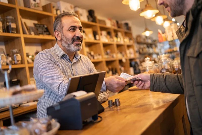 صاحب محل يُتمّ عملية بيع نقدية على نقطة البيع خلف الكاونتر